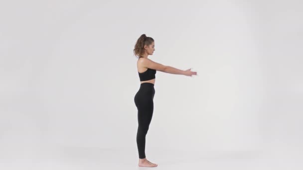 Jonge dame in zwart pak demonstratie Utkatasana yoga pose, hand opsteken en het doen van squat, volledige lengte portret — Stockvideo