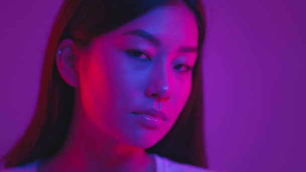 Красота молодости. Молодая корейская женщина улыбается в камеру, позируя в фиолетовых неоновых огнях на фоне фиолетовой студии — стоковое видео