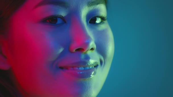 Jovem milenar mulher japonesa virando rosto para a câmera e sorrindo, posando em luzes de néon coloridas brilhantes, espaço livre — Vídeo de Stock