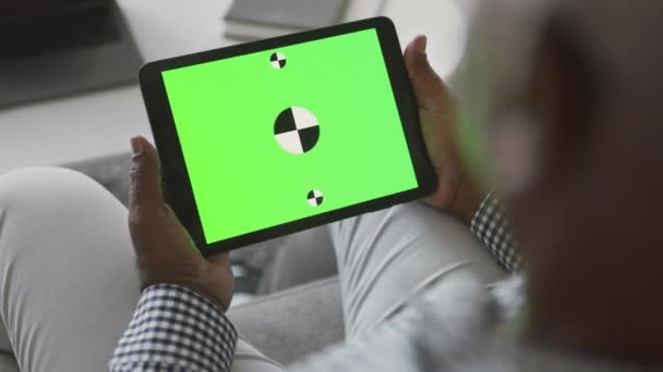 Над плечом вид цифрового планшета с зеленым цветным экраном ключа в руках старшего африканского мужчины, отслеживающий выстрел — стоковое видео