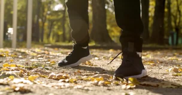 秋の公園でジャンプスニーカーを身に着けている男性の足のショットを閉じる,認識できない男の運動,スローモーション — ストック動画