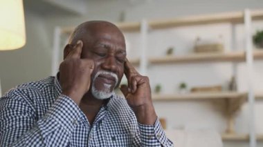 Kıdemli Afro-Amerikan adam şakaklarına masaj yapıyor, evinde baş ağrısı çekiyor, ağır çekimde, boş alanda.