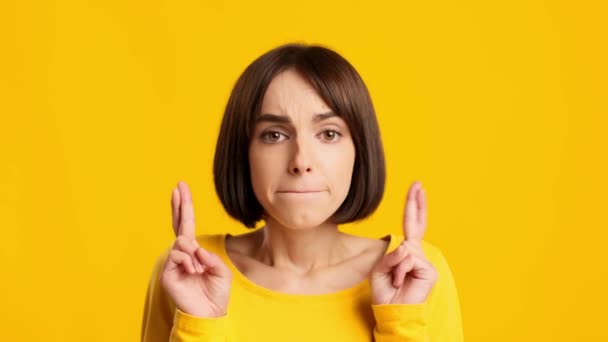 Тревожная леди держит пальцы скрещенными на удачу на жёлтом фоне — стоковое видео