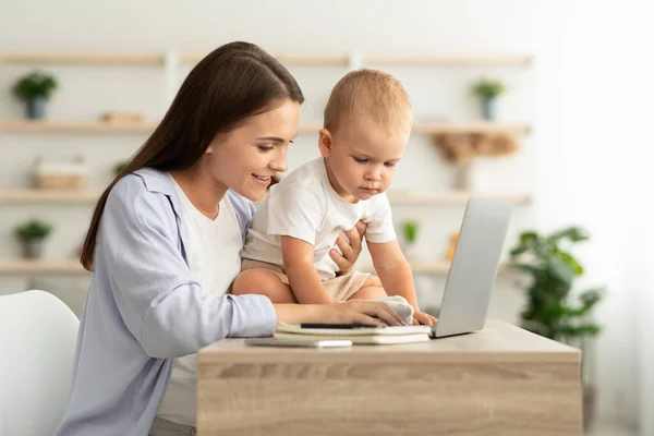 Jovem mulher trabalhando no laptop e cuidar do bebê em casa — Fotografia de Stock