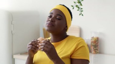 Sağlıksız beslenme. Şişman Siyah Kadın Spor Giyim Mutfakta Çizburger Yiyiyor