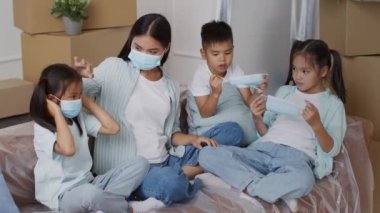 Taşınan kutuların arasında oturan Asyalı Aile Maskeleri Giyiyor