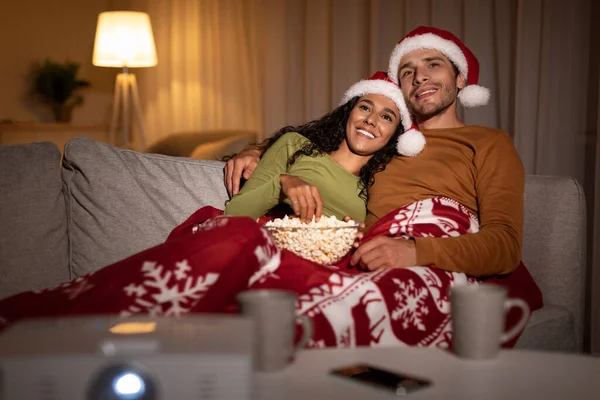 サンタの帽子をかぶったカップルが自宅でクリスマスを祝う映画を見る — ストック写真