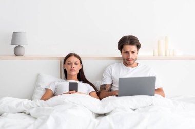 Milenyum Avrupalı ciddi çekici kadın ve erkek aletlerle sohbet ediyor, yatak odasında blog okuyor ya da yatakta haber okuyor.