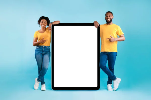 Καυτή προσφορά, online πώληση. Δροσερό μαύρο νεαρό ζευγάρι που δείχνει τον υπολογιστή tablet με χώρο mockup πάνω από το μπλε φόντο στούντιο — Φωτογραφία Αρχείου