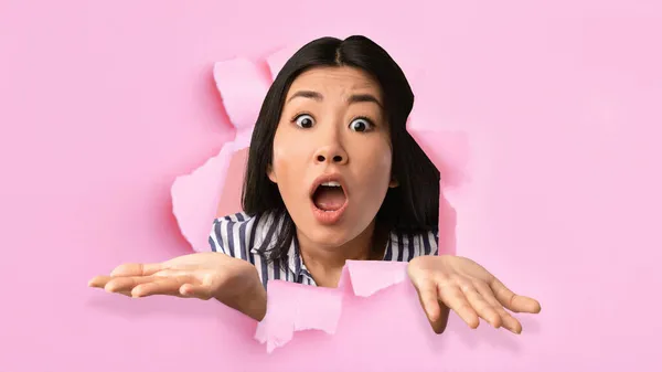 Pretty Asian woman looking through hole in torn pink paper, expressing exciement and surprise. Huge sale concept — Stock Photo, Image