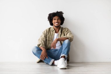 Beyaz duvarın yanında, yerde dinlenen gülümseyen yakışıklı zenci portresi.