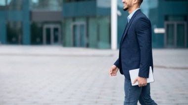 Elinde dijital tabletle sokakta yürüyen takım elbiseli tanınmayan bir adam.