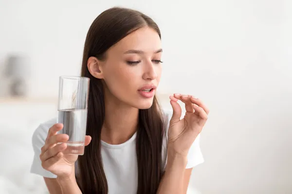 Millennial hübsche kaukasische Frau halten Pille und Glas Wasser im Schlafzimmer Interieur — Stockfoto