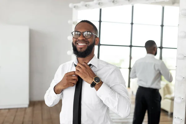 Lächelnder afroamerikanischer Geschäftsmann passt Krawatte in Spiegelnähe an — Stockfoto