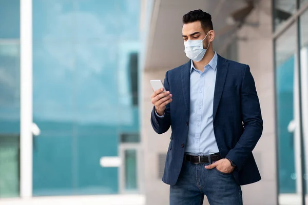 Empreendedor do Oriente Médio em máscara facial usando telefone enquanto caminha — Fotografia de Stock