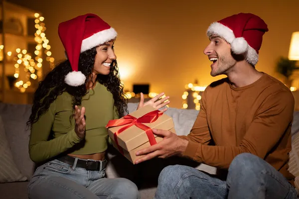 Муж дарит рождественский подарок жене, поздравляя ее дома — стоковое фото