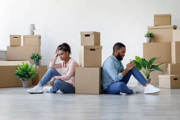 Ongelukkige jonge zwarte man en dame zijn moe en zitten op de vloer in appartement met dozen — Stockfoto