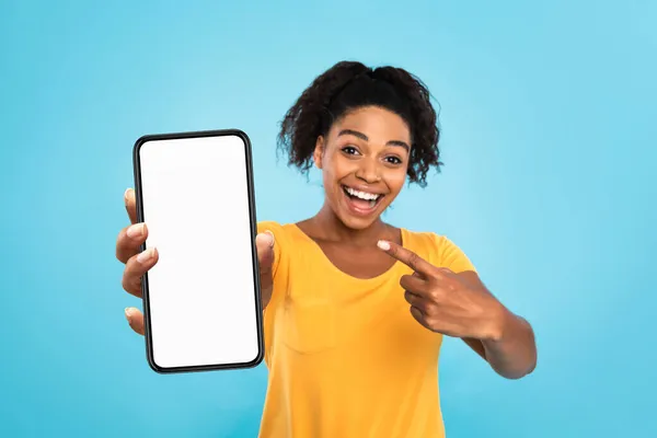 Sorridente signora nera che dimostra smartphone con mockup, puntando lo schermo vuoto su sfondo blu, spazio per app — Foto Stock