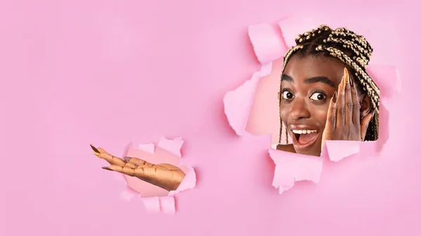 Megdöbbent fekete hölgy mutatja üres hely, megérinti az arcát izgalomban, néz át lyukon szakadt rózsaszín papír — Stock Fotó