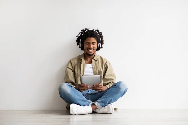 Jovem preto cara vestindo fones de ouvido sem fio relaxante no chão com Digital Tablet — Fotografia de Stock