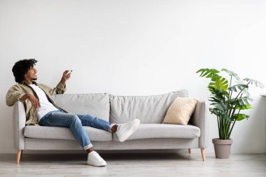 Siyah adam evdeki uzaktan kumandayla klimayı açıyor.