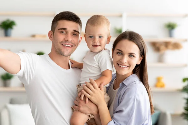 Jovem família feliz com o pequeno filho infantil tomando selfie juntos em casa — Fotografia de Stock