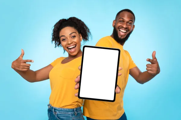 Pasangan hitam yang menunjuk pada layar tablet dengan mockup untuk desain, mengiklankan aplikasi baru atau situs web dengan latar belakang biru — Stok Foto