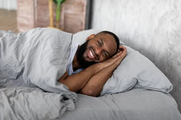 若いアフリカ系アメリカ人の男がベッドの上でカメラを見て — ストック写真