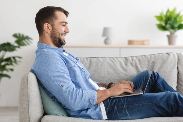 Feliz caucásico adulto hombre en casual relajarse en el sofá, navegar en Internet y charlar en el tiempo libre — Foto de Stock