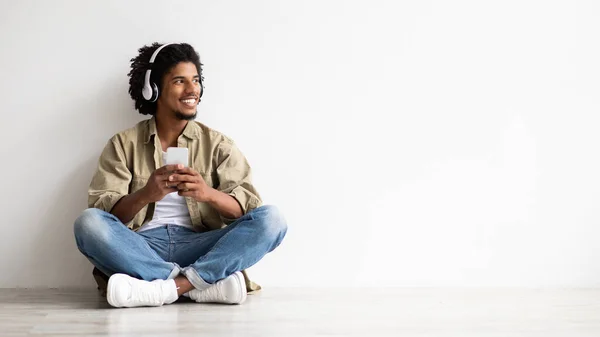Vidám fekete fickó használ okostelefon és vezeték nélküli fejhallgató hallgatásához zene Online — Stock Fotó