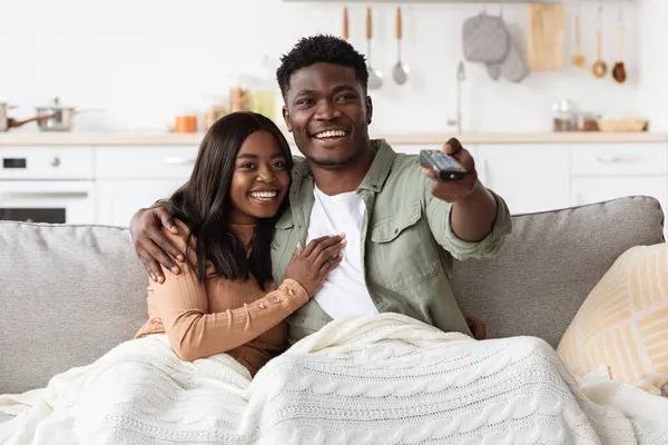 Joyful african american couple watching TV together at home