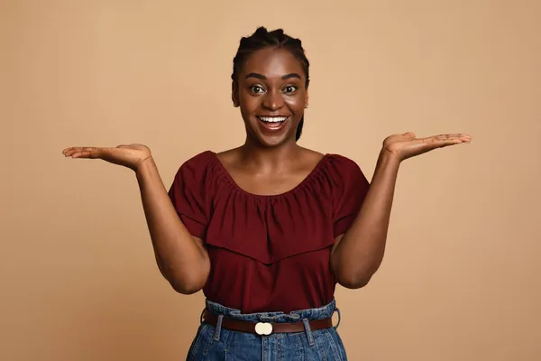 Verward Afro-Amerikaanse vrouw houdt iets onzichtbaar op beide handpalmen — Stockfoto