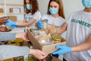 Maskeli genç gönüllüler konserve, kavanoz ve paketlere yiyecek dolduruyorlar. Fakir insanlara bağış olarak.