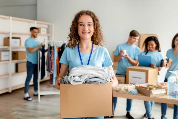 Dobrovolnická koncepce. Šťastná mladá žena v uniformě držení kartónové krabice s oblečením na dar — Stock fotografie