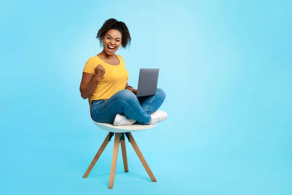 Cool jeune femme noire assise sur une chaise avec ordinateur portable, geste OUI, pari de casino gagnant ou jeu en ligne, shopping sur le web — Photo