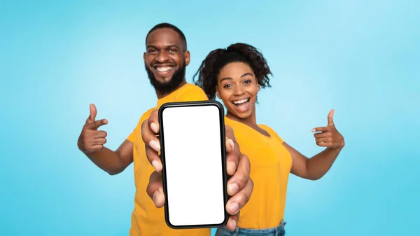 Lihat ini, mockup tampilan ponsel. Pasangan hitam ceria yang menunjuk ke ponsel dengan layar kosong pada latar belakang biru — Stok Foto