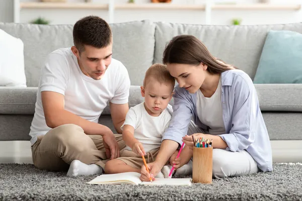 Jovens pais com adorável bebê infantil desenhando juntos em casa — Fotografia de Stock