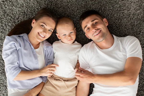 Genitori felici e bambino bambino sdraiato sul pavimento e sorridente alla fotocamera — Foto Stock