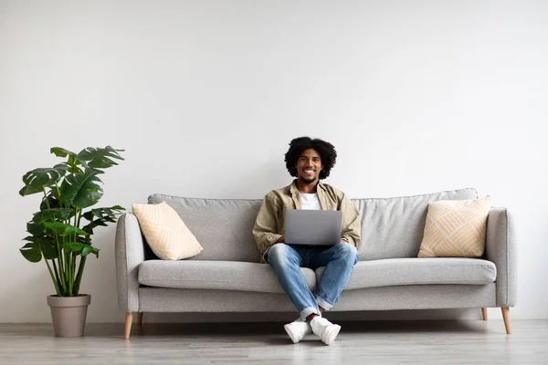 Retrato de bonito sorridente preto homem relaxante no sofá com laptop — Fotografia de Stock
