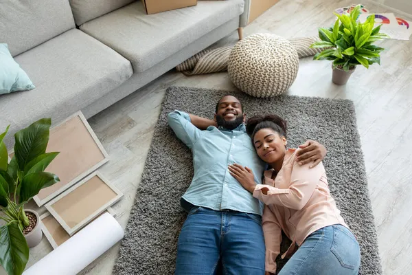 Satisfeita jovem família afro-americana deitar no chão, descansando depois de se mudar para novo apartamento na sala de estar — Fotografia de Stock