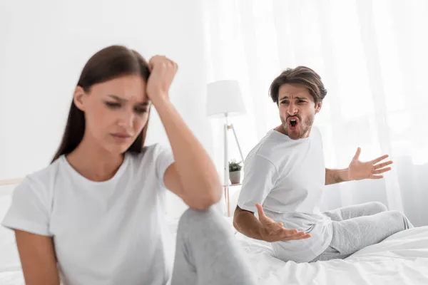Agresivo malvado milenario marido caucásico con gritos de rastrojo y jura ofendida triste esposa deprimida en el dormitorio —  Fotos de Stock