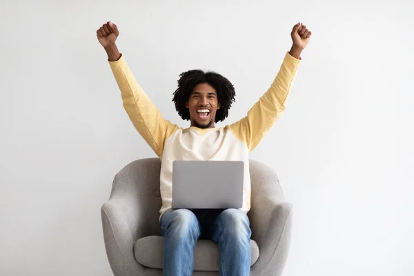 Online winnen. Happy Black Guy viert succes met laptop, zitten in stoel — Stockfoto