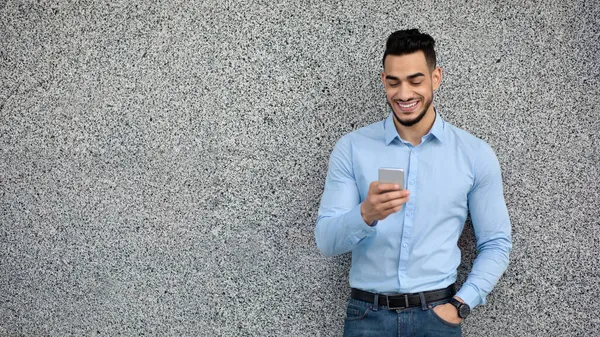 Wesoły arabski facet pracownik za pomocą telefonu komórkowego, szary tle ściany — Zdjęcie stockowe