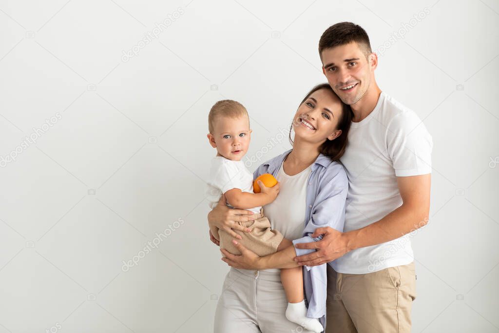 Happy Young Parents Holding Their Cute Toddler Son And Smiling At Camera