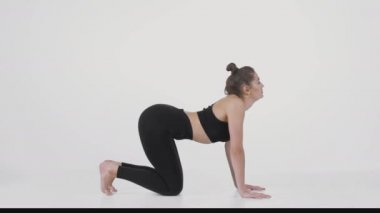 Sırt güçlendirme pratiği. Kedi ineği pozu veren, beyaz arka planda diz çökmüş, esnek, genç bayanın yan görüntüsü.