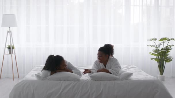 Due giovani sorelle nere che indossano accappatoi rilassanti sul letto a casa — Video Stock