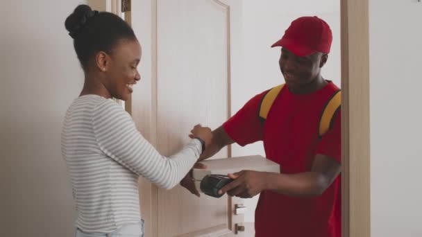 Souriant homme noir messager gars portant uniforme rouge tenant des boîtes à pizza, femme afro-américaine payer avec smartphone — Video