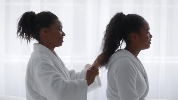 Заботливая молодая африканская американка расчесывает волосы своей прекрасной сестры-подростка — стоковое видео