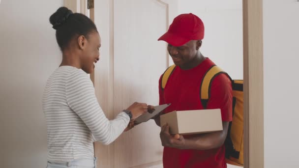 安全な配達の概念。若いアフリカ系アメリカ人女性は、個人的な注文のために署名し、ブラック宅配便からパッケージボックスを取得 — ストック動画