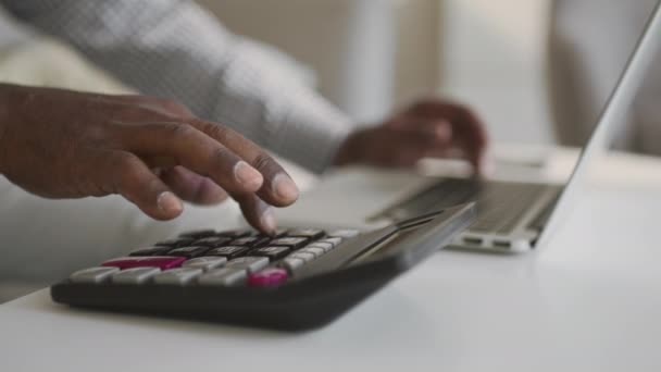 Comptable afro-américain masculin méconnaissable faisant rapport financier en ligne, travaillant sur calculatrice et ordinateur portable à la maison — Video